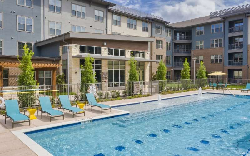 A pool with tanning deck and white chairs