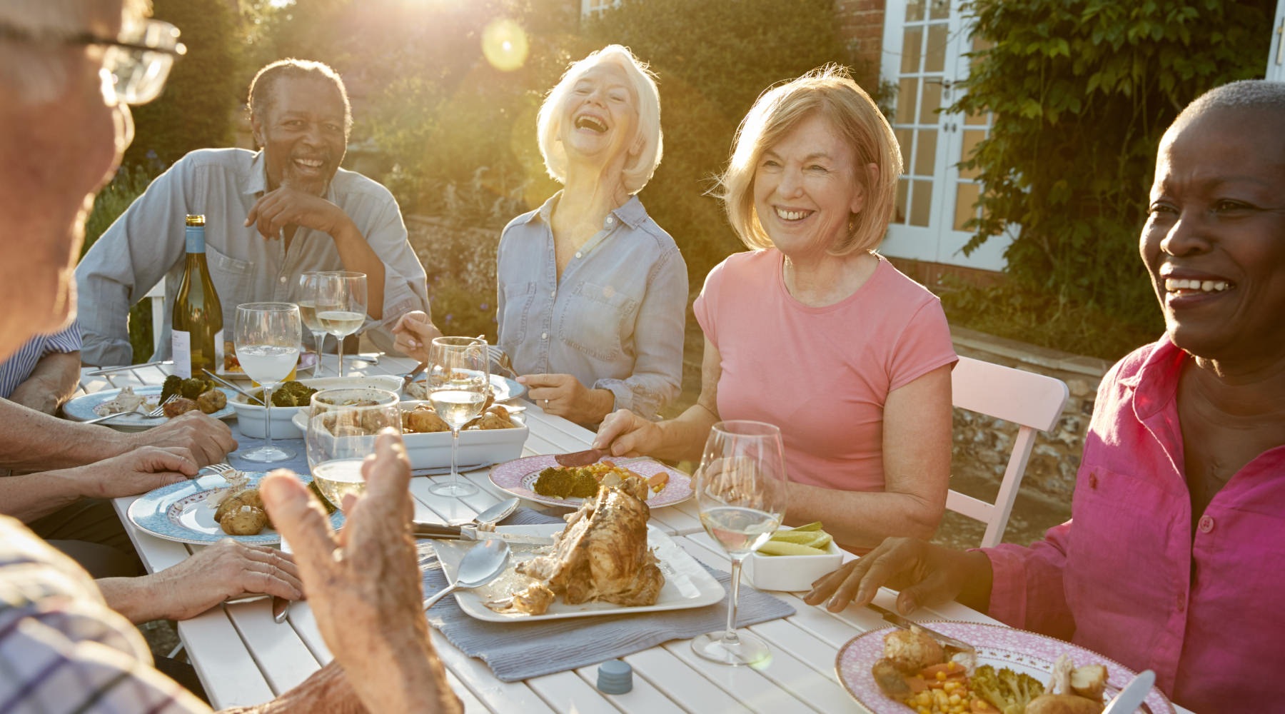 Friends gathering for dinner People dining outside at The Orchards at Market Plaza senior living community in Plano, TX, featuring warm sunlight.